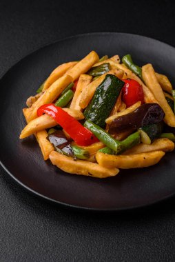 Lezzetli kızarmış patates, dolmalık biber, kuşkonmaz fasulyesi, tuz ve baharatlar, koyu beton bir arka planda.