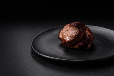 Tuzlu biftek, baharat ve otlar seramik tabakta koyu beton arka planda.