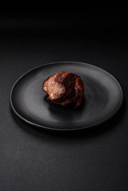 Tuzlu biftek, baharat ve otlar seramik tabakta koyu beton arka planda.