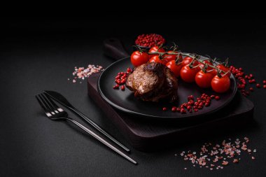 Tuzlu biftek, baharat ve otlar seramik tabakta koyu beton arka planda.