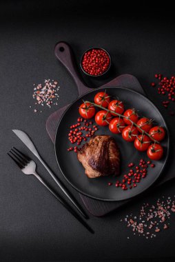 Tuzlu biftek, baharat ve otlar seramik tabakta koyu beton arka planda.