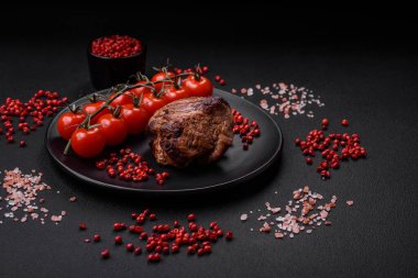 Tuzlu biftek, baharat ve otlar seramik tabakta koyu beton arka planda.