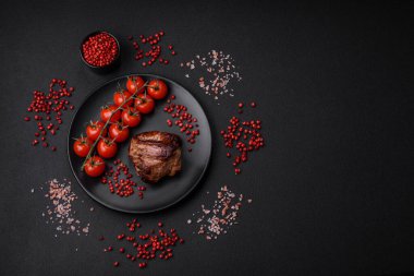 Tuzlu biftek, baharat ve otlar seramik tabakta koyu beton arka planda.