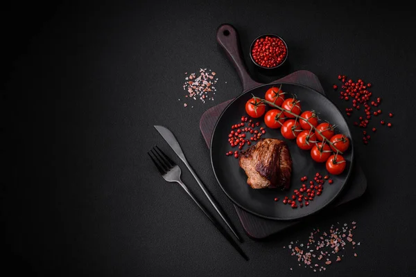 stock image Delicious beef steak with salt, spices and herbs on a ceramic plate on a dark concrete background