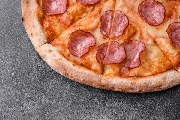 stock image Tasty fresh pizza with salami, cheese, tomatoes, spices and salt on a dark concrete background