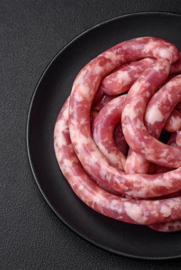 Koyu beton arka planda tuzlu, baharatlı ve otlu domuz eti ya da biftekten çiğ sosis.