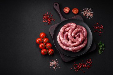 Koyu beton arka planda tuzlu, baharatlı ve otlu domuz eti ya da biftekten çiğ sosis.