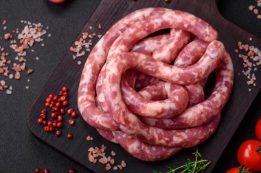 Koyu beton arka planda tuzlu, baharatlı ve otlu domuz eti ya da biftekten çiğ sosis.