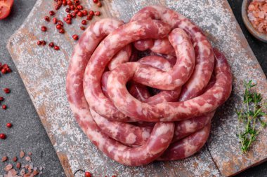 Koyu beton arka planda tuzlu, baharatlı ve otlu domuz eti ya da biftekten çiğ sosis.