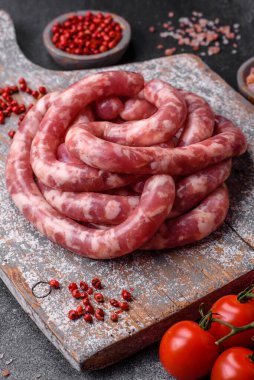 Koyu beton arka planda tuzlu, baharatlı ve otlu domuz eti ya da biftekten çiğ sosis.