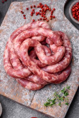 Koyu beton arka planda tuzlu, baharatlı ve otlu domuz eti ya da biftekten çiğ sosis.