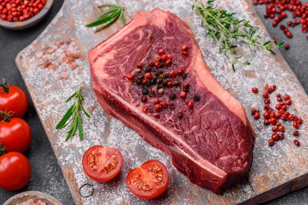 stock image Fresh juicy raw new york beef steak with salt, spices and herbs on dark concrete background