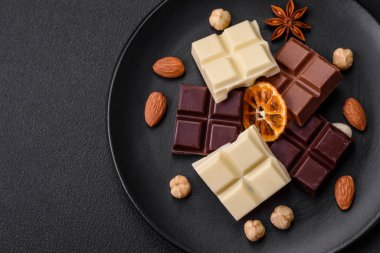 Koyu beton bir arka planda siyah bir tabakta parçalanmış çeşitli lezzetli çikolataların karışımı.