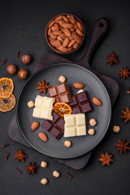 Koyu beton bir arka planda siyah bir tabakta parçalanmış çeşitli lezzetli çikolataların karışımı.