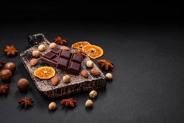 stock image Delicious sweet black chocolate broken into cubes on a wooden cutting board on a dark concrete background