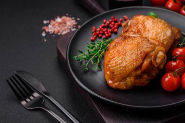 Tuz, baharat ve otlarla pişirilmiş lezzetli sulu tavuk butları koyu beton arka planda seramik bir tabakta.