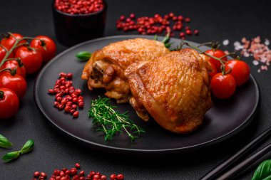 Tuz, baharat ve otlarla pişirilmiş lezzetli sulu tavuk butları koyu beton arka planda seramik bir tabakta.