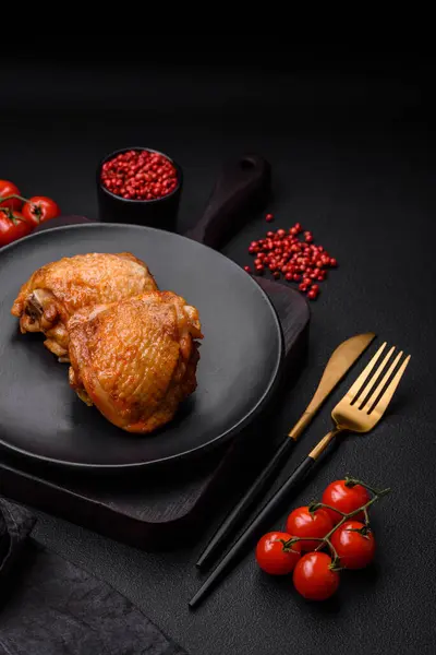 stock image Delicious juicy chicken thighs baked with salt, spices and herbs in a ceramic plate on a dark concrete background