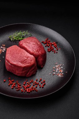 Tuz, baharat ve otlarla çevrili çiğ biftek, dokulu bir arka planda ızgara için hazırlandı.