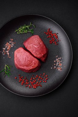 Tuz, baharat ve otlarla çevrili çiğ biftek, dokulu bir arka planda ızgara için hazırlandı.