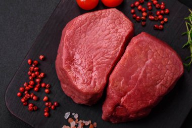 Tuz, baharat ve otlarla çevrili çiğ biftek, dokulu bir arka planda ızgara için hazırlandı.