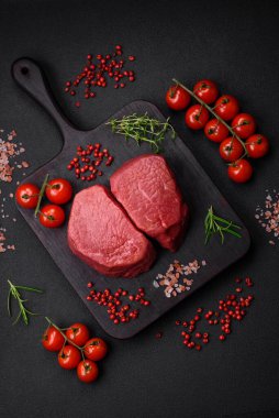Tuz, baharat ve otlarla çevrili çiğ biftek, dokulu bir arka planda ızgara için hazırlandı.