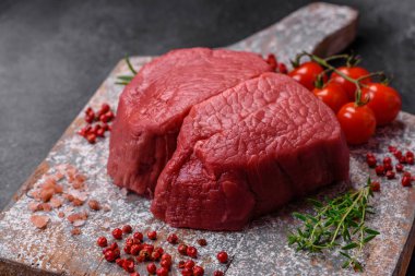 Tuz, baharat ve otlarla çevrili çiğ biftek, dokulu bir arka planda ızgara için hazırlandı.