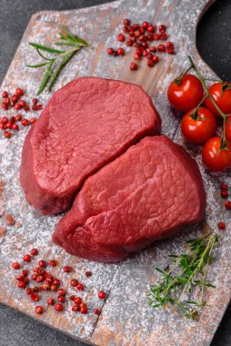 Tuz, baharat ve otlarla çevrili çiğ biftek, dokulu bir arka planda ızgara için hazırlandı.