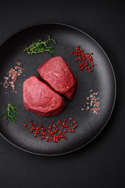 Tuz, baharat ve otlarla çevrili çiğ biftek, dokulu bir arka planda ızgara için hazırlandı.