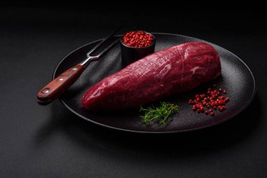 Koyu beton arka planda baharatlı, tuzlu ve otlu sulu çiğ biftek. Et yemeği pişirmeye hazırlanıyor.