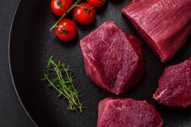 Koyu beton arka planda baharatlı, tuzlu ve otlu sulu çiğ biftek. Et yemeği pişirmeye hazırlanıyor.