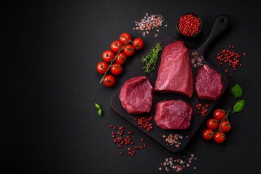 Koyu beton arka planda baharatlı, tuzlu ve otlu sulu çiğ biftek. Et yemeği pişirmeye hazırlanıyor.