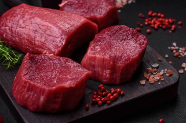 Koyu beton arka planda baharatlı, tuzlu ve otlu sulu çiğ biftek. Et yemeği pişirmeye hazırlanıyor.