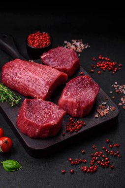Koyu beton arka planda baharatlı, tuzlu ve otlu sulu çiğ biftek. Et yemeği pişirmeye hazırlanıyor.