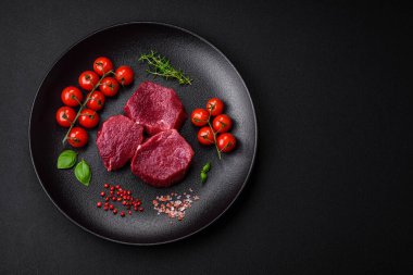 Koyu beton arka planda baharatlı, tuzlu ve otlu sulu çiğ biftek. Et yemeği pişirmeye hazırlanıyor.