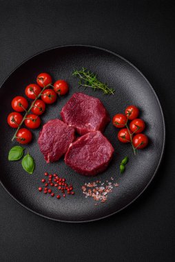 Koyu beton arka planda baharatlı, tuzlu ve otlu sulu çiğ biftek. Et yemeği pişirmeye hazırlanıyor.