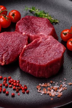 Koyu beton arka planda baharatlı, tuzlu ve otlu sulu çiğ biftek. Et yemeği pişirmeye hazırlanıyor.