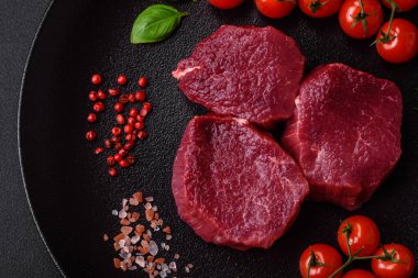 Koyu beton arka planda baharatlı, tuzlu ve otlu sulu çiğ biftek. Et yemeği pişirmeye hazırlanıyor.