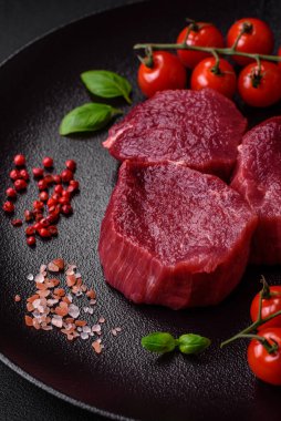 Koyu beton arka planda baharatlı, tuzlu ve otlu sulu çiğ biftek. Et yemeği pişirmeye hazırlanıyor.