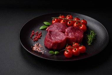 Koyu beton arka planda baharatlı, tuzlu ve otlu sulu çiğ biftek. Et yemeği pişirmeye hazırlanıyor.
