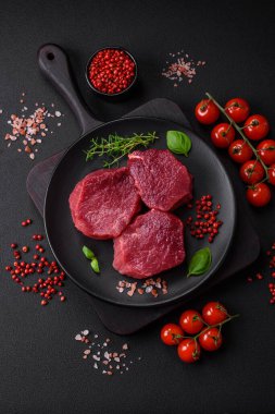 Koyu beton arka planda baharatlı, tuzlu ve otlu sulu çiğ biftek. Et yemeği pişirmeye hazırlanıyor.