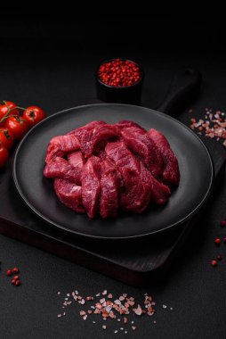 Koyu beton arka planda baharatlı, tuzlu ve otlu sulu çiğ biftek. Et yemeği pişirmeye hazırlanıyor.