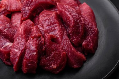 Koyu beton arka planda baharatlı, tuzlu ve otlu sulu çiğ biftek. Et yemeği pişirmeye hazırlanıyor.