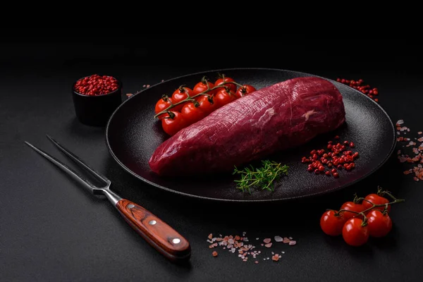 stock image Juicy raw beef with spices, salt and herbs on a dark concrete background. Preparing to cook a meat dish