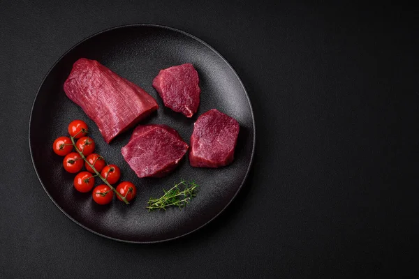 stock image Juicy raw beef with spices, salt and herbs on a dark concrete background. Preparing to cook a meat dish