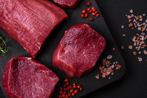 Juicy raw beef with spices, salt and herbs on a dark concrete background. Preparing to cook a meat dish