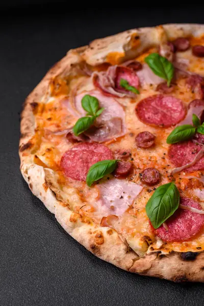 stock image Delicious fresh oven baked pizza with salami, meat, cheese, tomatoes, spices and herbs on a dark concrete background