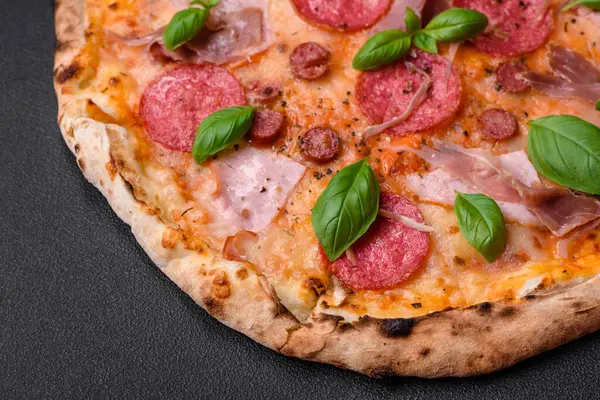 stock image Delicious fresh oven baked pizza with salami, meat, cheese, tomatoes, spices and herbs on a dark concrete background