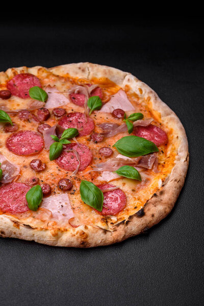 Delicious fresh oven baked pizza with salami, meat, cheese, tomatoes, spices and herbs on a dark concrete background