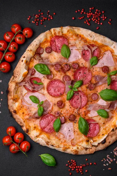 stock image Delicious fresh oven baked pizza with salami, meat, cheese, tomatoes, spices and herbs on a dark concrete background